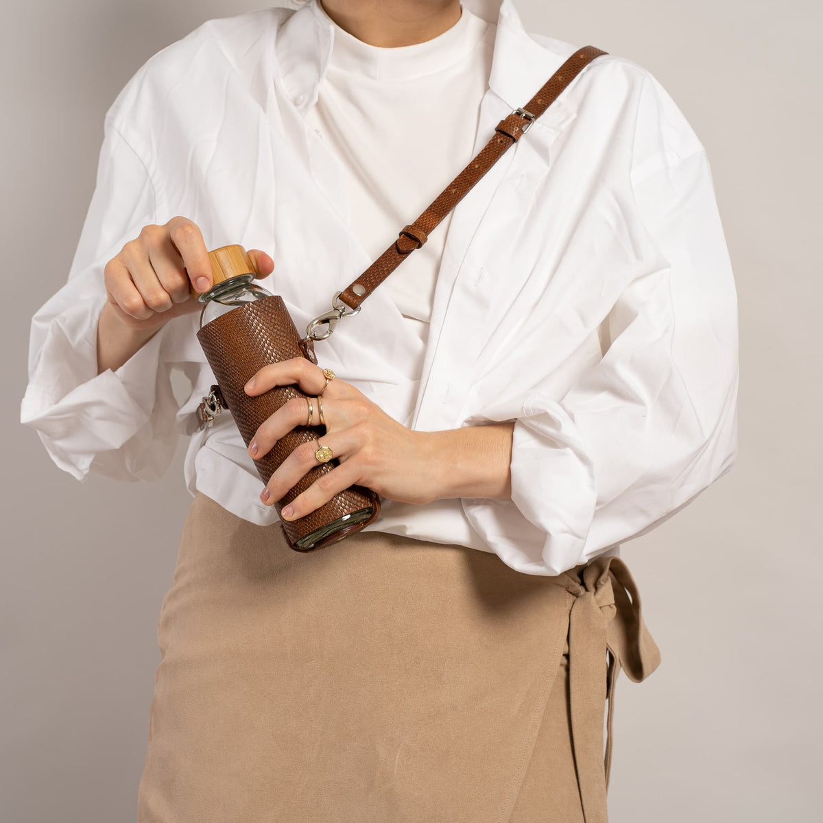 Leather water bottle holder with strap and glass bottle.