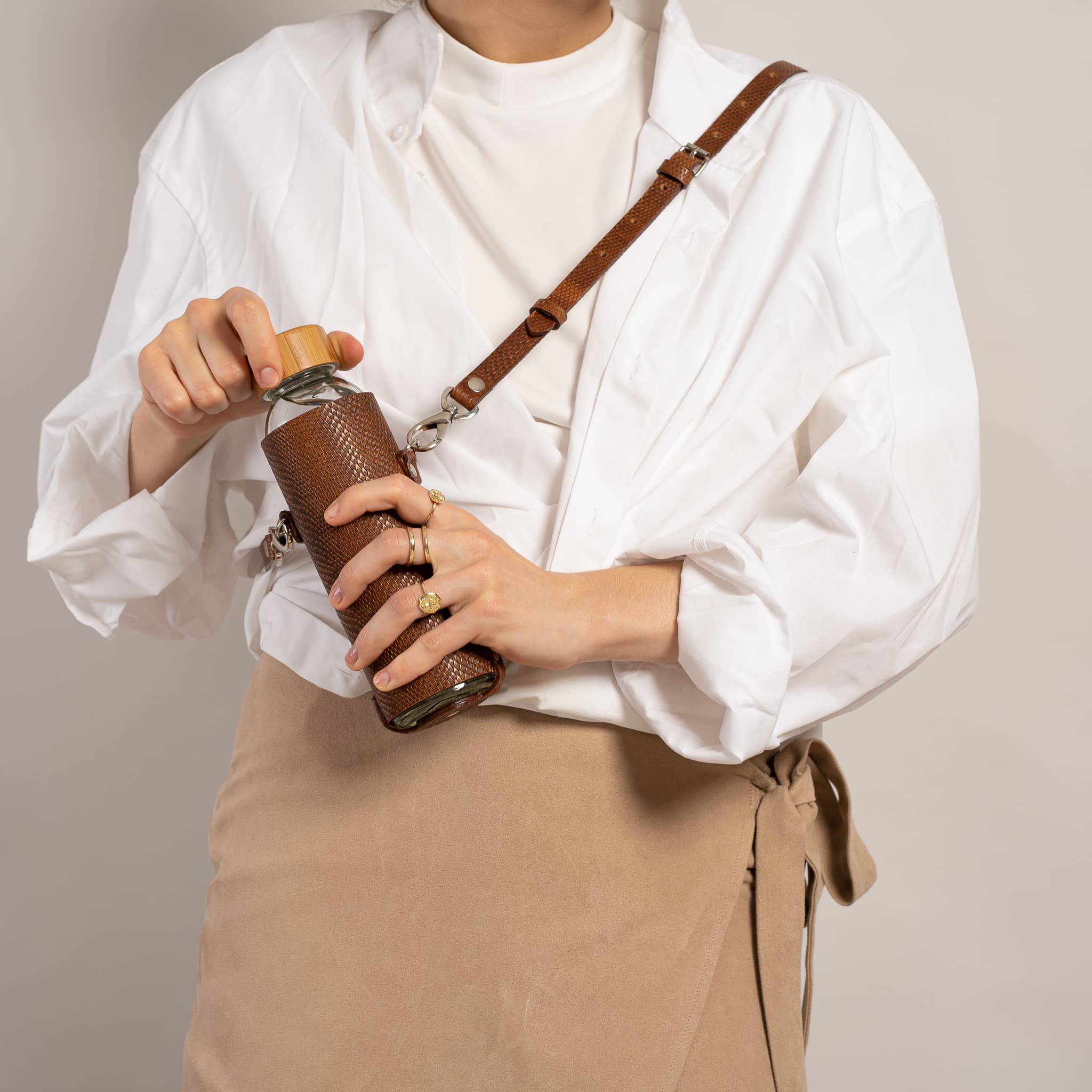 Leather water bottle holder with strap and glass bottle.