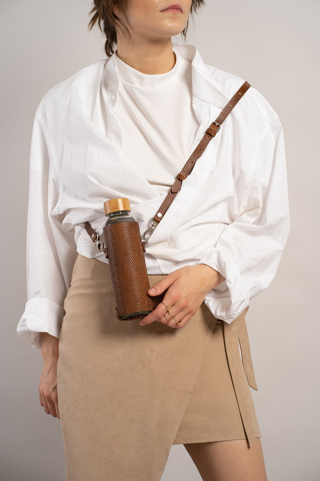 Leather water bottle holder with strap and glass bottle.