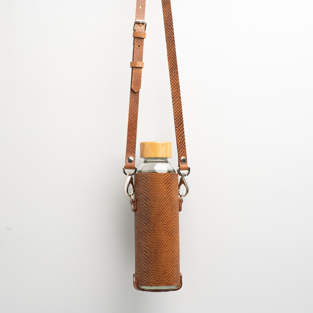 Leather water bottle holder with strap and glass bottle.