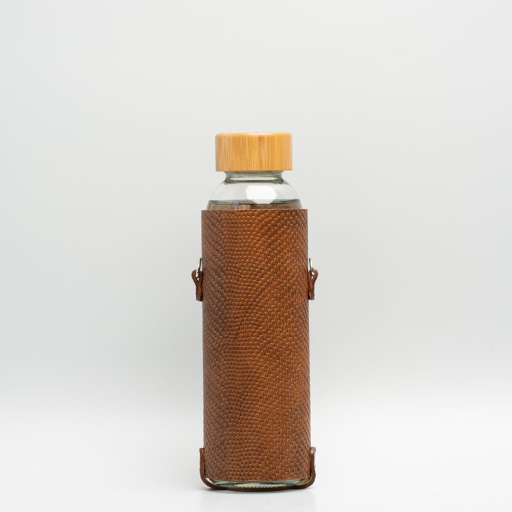 Leather water bottle holder with strap and glass bottle.