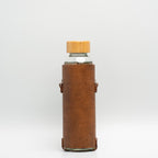 Leather water bottle holder with strap and glass bottle.