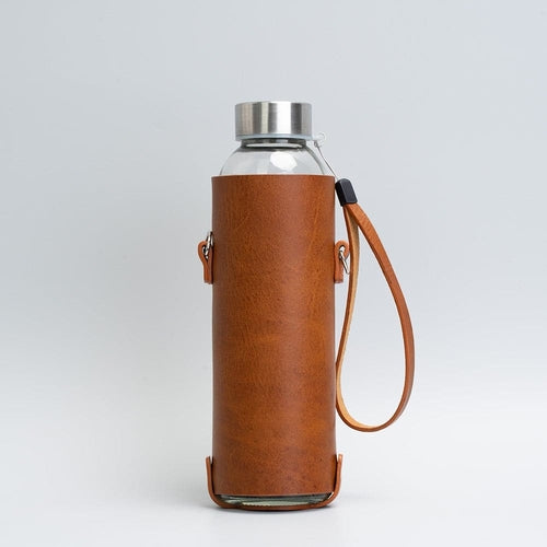 Leather water bottle holder with strap and glass bottle.