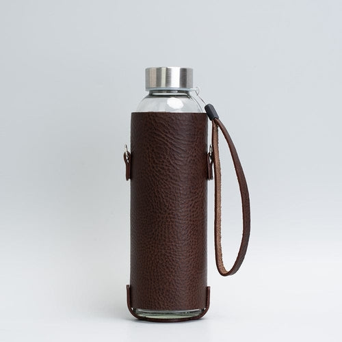 Leather water bottle holder with strap and glass bottle.